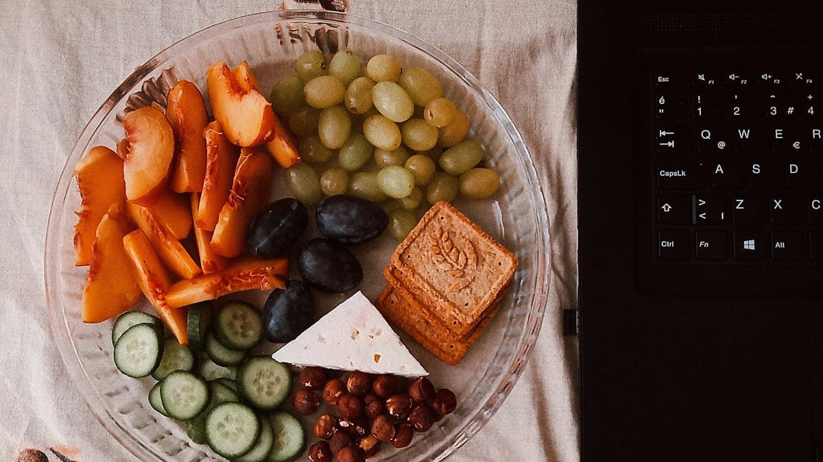 A delightful snack plate with fruits, cheese, and a laptop for a healthy lifestyle.