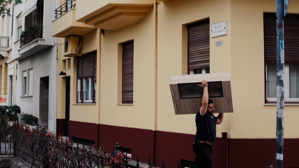 Photo of a man carrying a large box on a city street near colorful buildings.